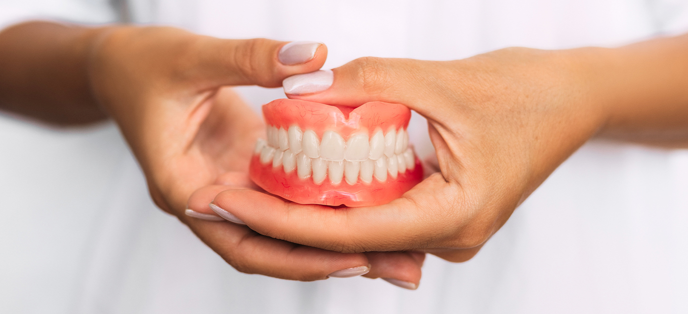 Manos sosteniendo unas prótesis dentales fijas  