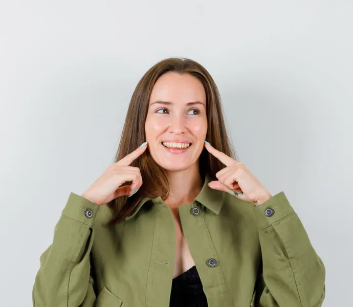 Mujer sonriendo con los dedos sobre la mandíbula tras tratar su bruxismo